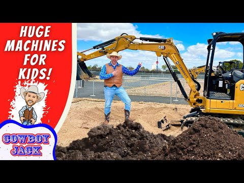 Man in cowboy outfit points at a CAT excavator on a construction site beside dirt piles and a red 'Huge Machines for Kids' banner.