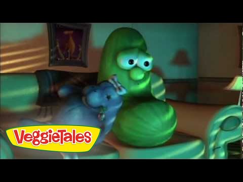 Green cucumber character from VeggieTales standing in a living room with a blue vegetable beside him; VeggieTales logo appears in the bottom-left corner.