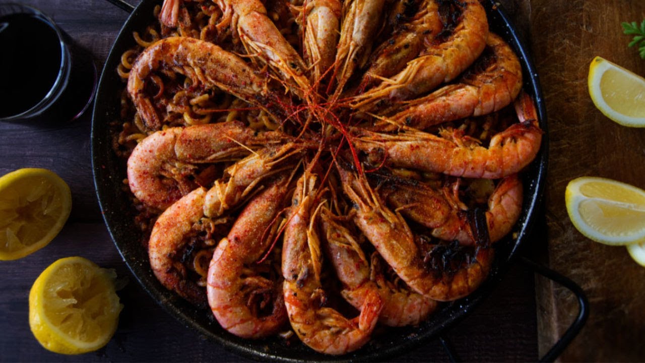 a large pan of fideua with seafood is topped with large shrimp
