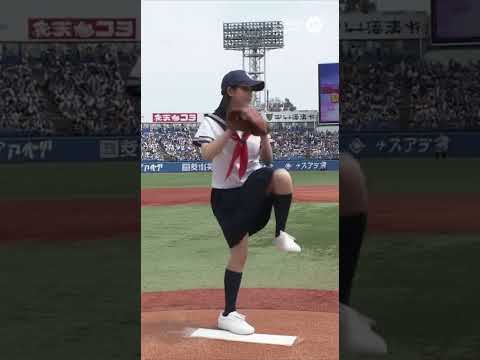 日本の女子高校生が野球の試合で始球式を行い、捕手に向かってボールを投げる。