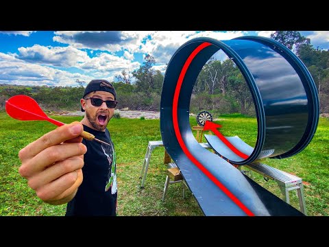 Man outdoors with a surprised expression holds a red dart toward a large looping metal slide and a small dartboard at the end.