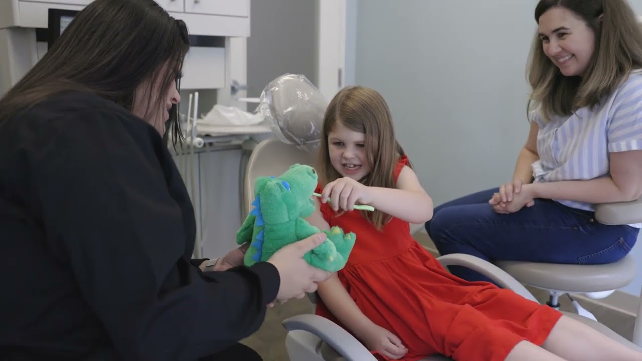 Young girl in dental chair brushing the teeth of a plush dinosaur