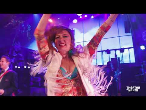 Rock of Ages stage musical trailer still with ensemble striking hair-metal poses under neon