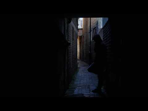 Man in hoddie in dark alleyway smoking