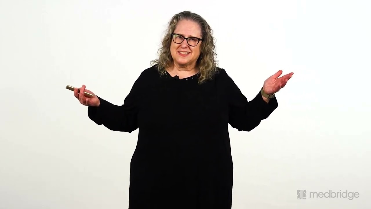 A woman with curly hair and glasses in black stands arms open, welcoming, in front of a white background for medbridge training.