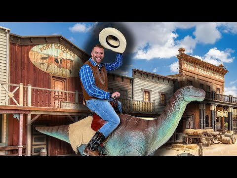 Man in a plaid shirt and brown vest rides a dinosaur statue through a Wild West street, tipping his hat cheerfully.