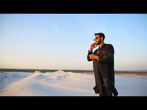 Handsome male Arab businessman talks on cellular business pro, standing in middle of sandy desert in