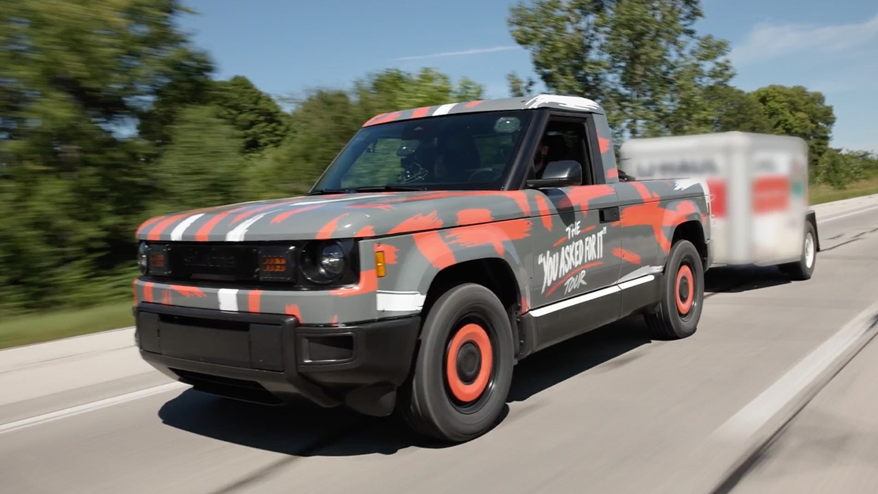 A Slate electric pickup loaded with boxes and towing a trailer
