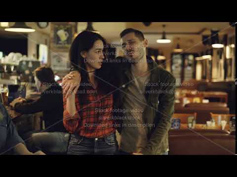 Young brunette is leading her drunk husband out of bar. Unshaven handsome young man is talking to