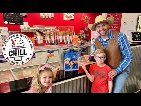 Smiling man in a cowboy hat and brown vest poses with two kids at an ice cream shop counter.