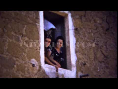 1954: Pretty Italian women waves stone construction building window. CIANCIANA, SICILY