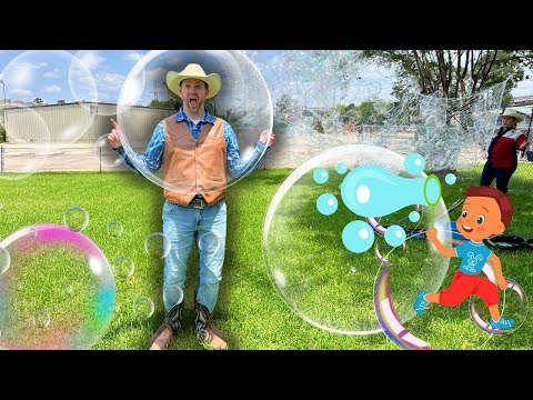 Man in a cowboy hat and vest poses on a grassy field, surrounded by giant bubbles and a cartoon boy drawing bubbles on the right side.