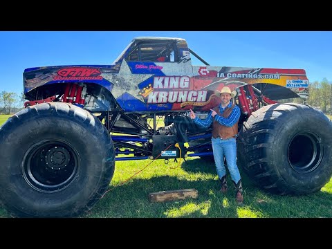Man in cowboy hat and vest stands next to a giant monster truck named King Krunch on a grassy field.