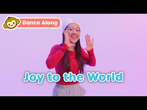 Smiling woman in a red sweatshirt waves with a purple background and the bold blue 'Joy to the World' text overlay; top-left 'Dance Along' badge present.