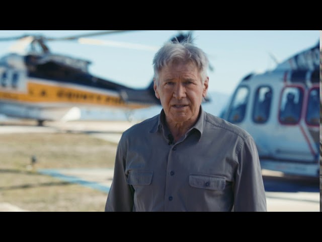 Harrison Ford standing in front of two fire helicopters