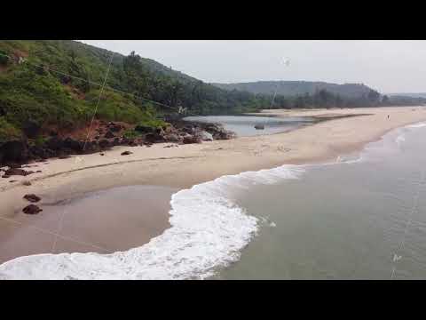 a girl stands on black rocks by the sea on a wild beach, aerial photography