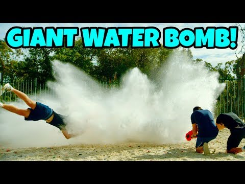 People outdoors get soaked by a huge water explosion; one person is mid‑air from the splash while two others kneel nearby with a water container. Bold text reads 'GIANT WATER BOMB!'