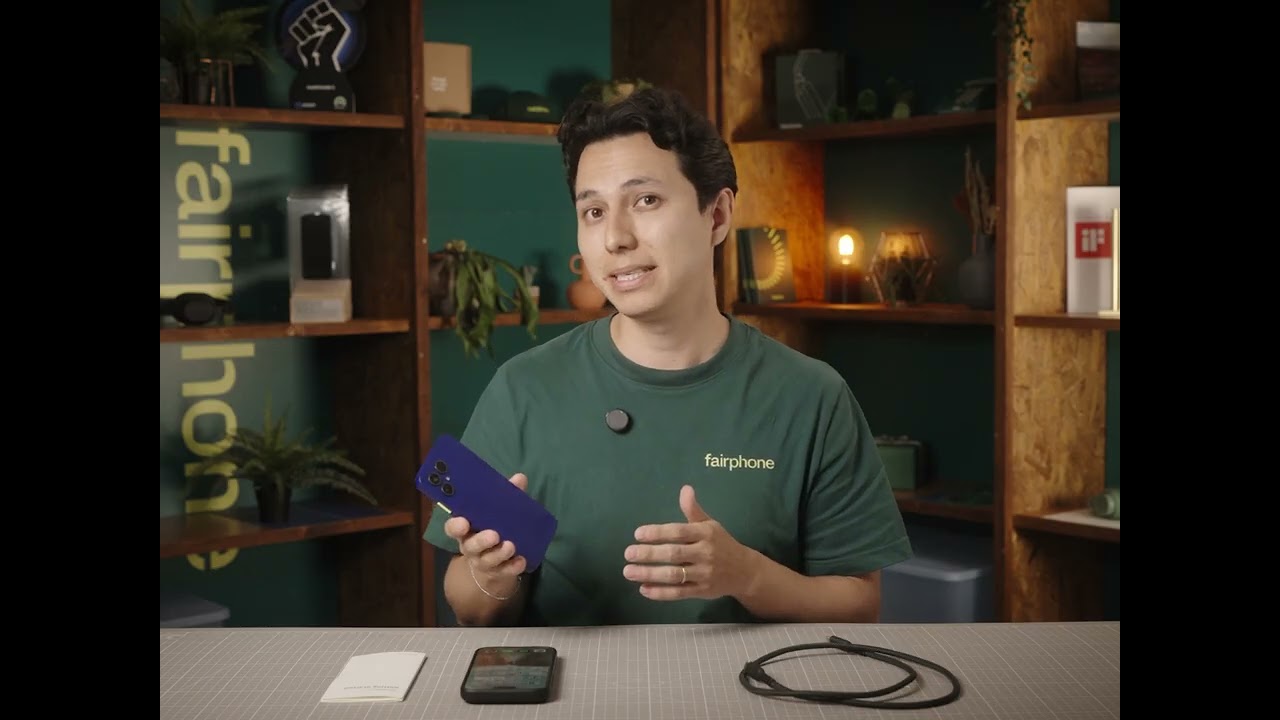 Fairphone presenter in a green Fairphone t-shirt holding up a blue Fairphone Gen 6+ to the camera