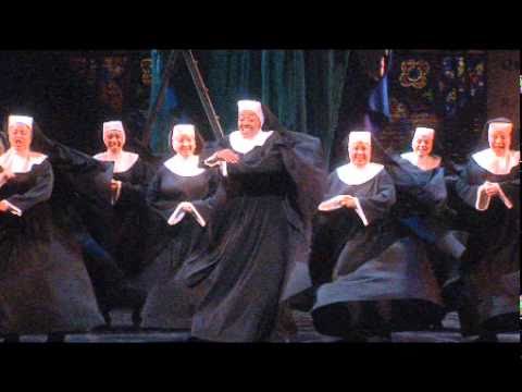 Trailer frame of the London Palladium set: gilded proscenium, neon club sign, and choir risers ready for Menken’s score