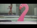 Inflatable Rubber Pink Flamingo Floating In A Pool On The Background Of A Passing Beauti