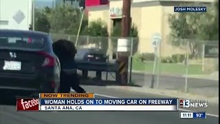 Woman holds on to moving car on freeway