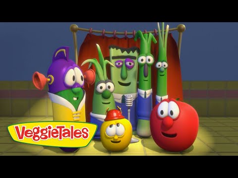 Group of VeggieTales vegetable characters posing together on a stage with a microphone and red curtain, smiling at the camera.