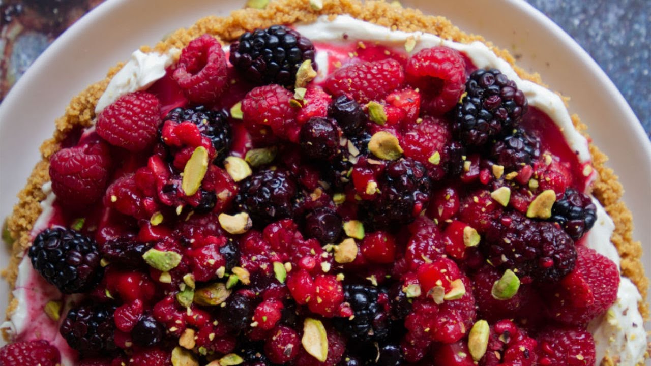 a large mixed berry cheesecake garnished with crushed pistachio nuts