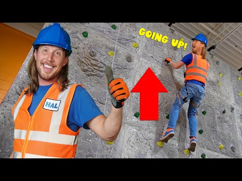 Climber in an orange safety vest and blue helmet ascends a rock-climbing wall, while another worker faces the camera and smiles with a thumbs up; a red arrow and 'GOING UP!' text appear.