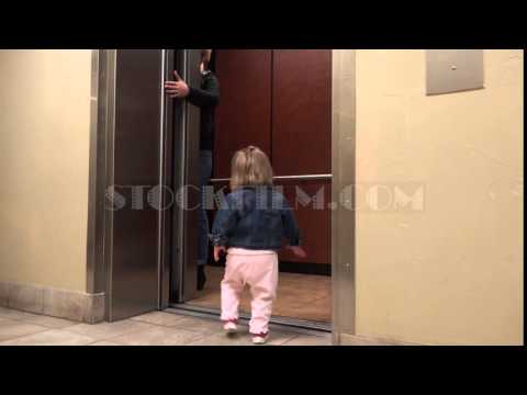 Mom holding elevator door for toddler entering hospital hallway.    DENVER, COLORADO