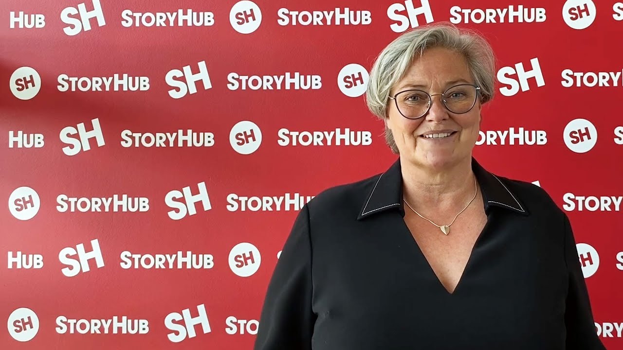 Clare Tomlinson, Sky Sport presenter, sits in front of a branded red and white StoryHub background
