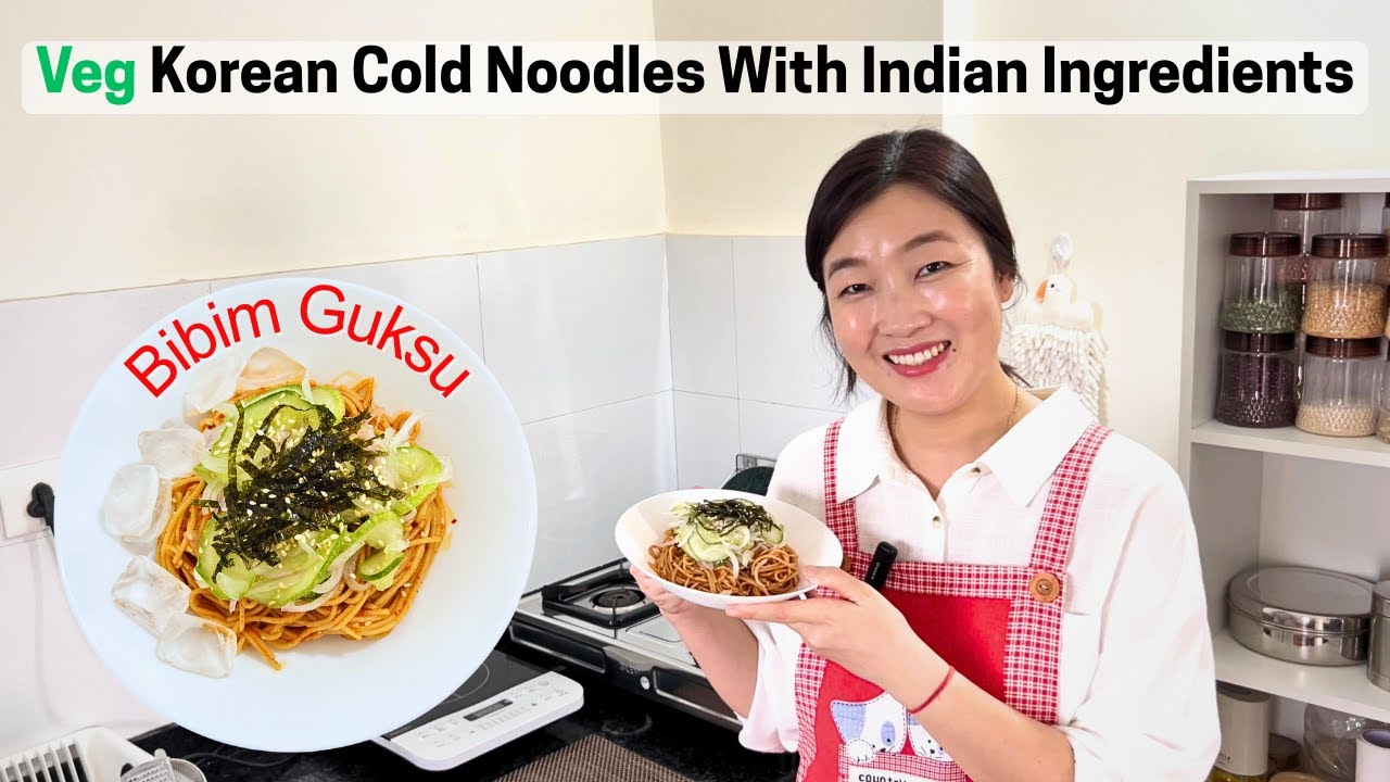 A plate of Korean bibim myeon spicy cold mixed noodles topped with red gochujang sauce cucumber strips and a half boiled egg