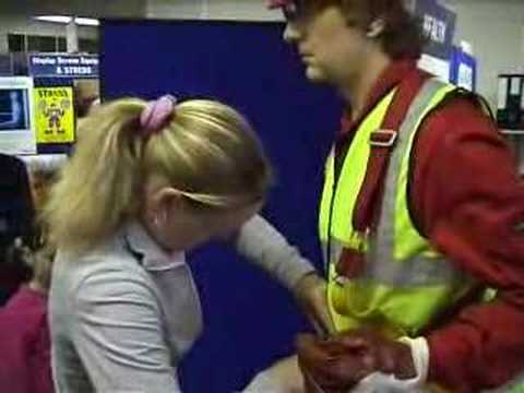 Safety harness competition joke with living mannequin #3 (flash) mannequin-man performming as a Living Mannequin: Fall arrest harness being put onto mannequin man by member of the public at a Safety clothing and PPE exhibition by ARCO at family open day at BAE (British Aerospace Engineering) systems in Rochester #3 (flash) for Arco on 06/07/2002