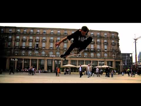 Trailer still: skater carving along a rural highway with mountains in the distance