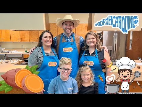 Group photo of four people in a kitchen, all wearing blue aprons with a sweet potato logo, smiling at the camera.