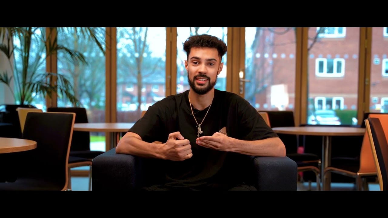 A man sat on a chair talking and looking at the camera