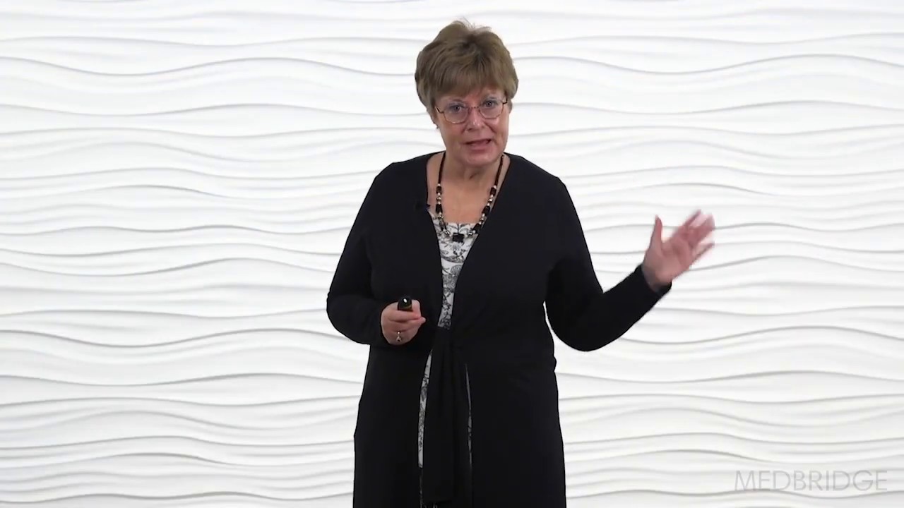 A person with short hair and glasses passionately discusses digital healthcare in front of a textured wall.