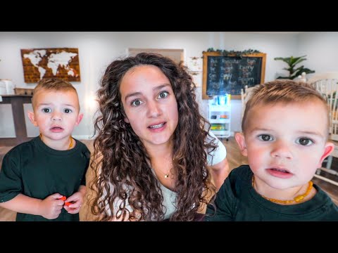 Mother with curly hair leaning toward the camera, flanked by two young boys in green shirts in a bright playroom; world map and chalkboard in the background.