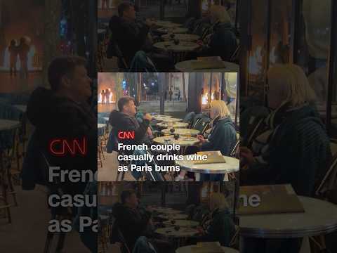 French couple casually drinks wine as Paris burns