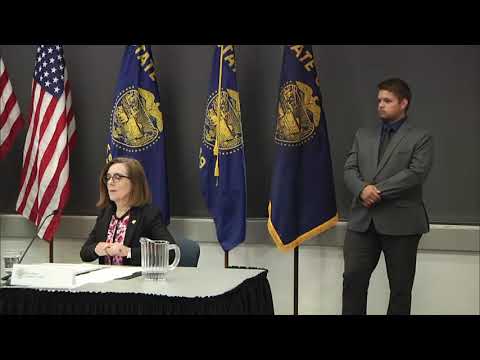 Governor Kate Brown holding a mask with one sign language intepretor standing behind her.