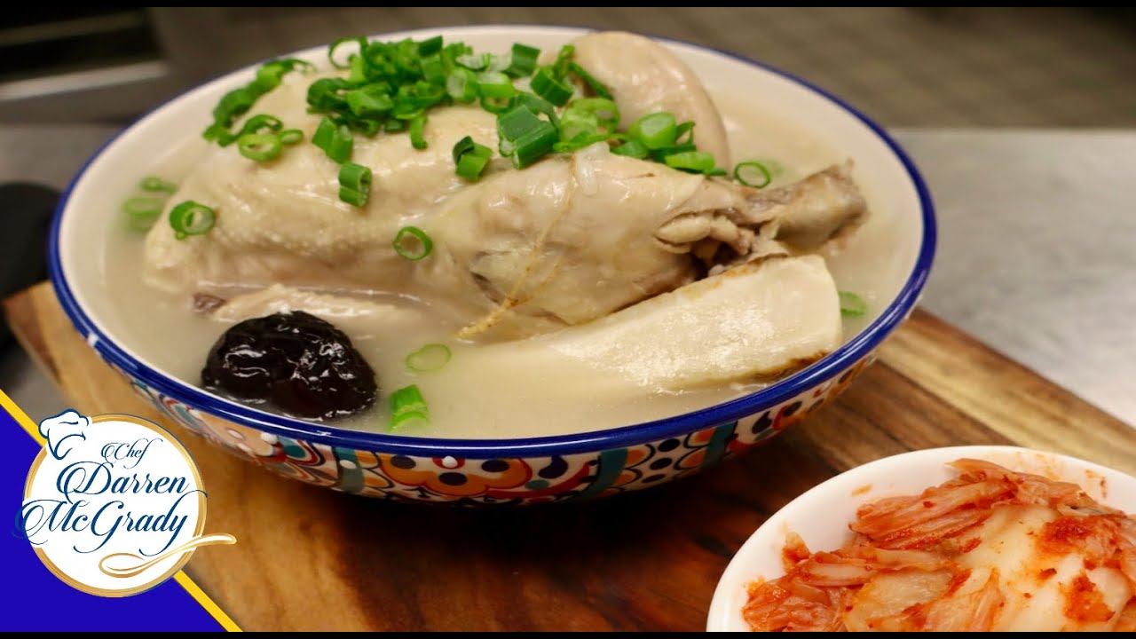 A ttukbaegi stone pot bowl of Korean samgyetang ginseng chicken soup with whole chicken floating in clear broth garnished with green onions