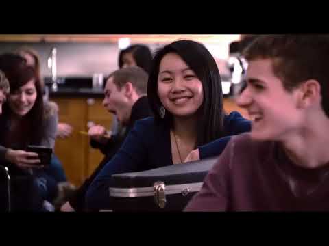 Trailer frame cutting from classroom chalkboard to roaring crowd, illustrating the film’s school-to-octagon musical pivot