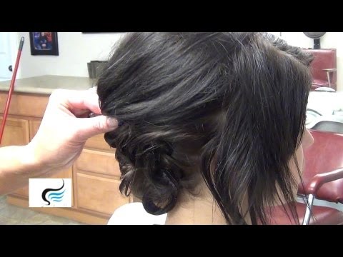 Close-up of a hairstylist shaping a low bun with pin curls on a model's dark hair, demonstrating techniques for a polished prom or wedding updo.