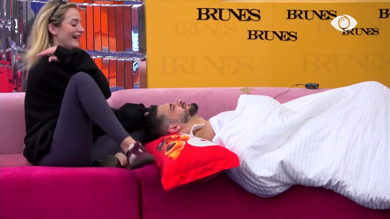 Selin dhe Gimbo qëndrojnë së bashku në dhomën e ndenjes, banorja i bën masazh