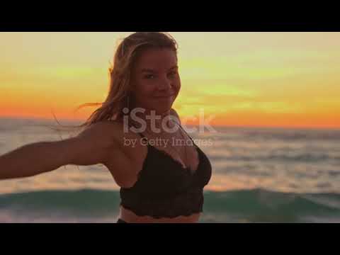 Slow motion shot of a young woman performs slow dancing moves on the beach at sunset.