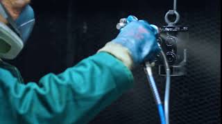 Man in PPE spraying coating a steel part 01