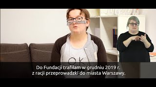 Na pierwszym planie widać panią Marię. Ma włosy średniej długości, okulary i przyłbicę. Na dole, na czarnym pasku znajdują się napisy - transkrypcja jej wypowiedzi.W prawym, dolnym rogu widać sylwetkę tłumacza PJM.