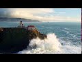 aerial view of lighthouse on cliff overlooking giant ocean waves under evening sky