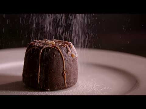 Slow motion clip of icing sugar being sprinkled on a chocolate dessert.