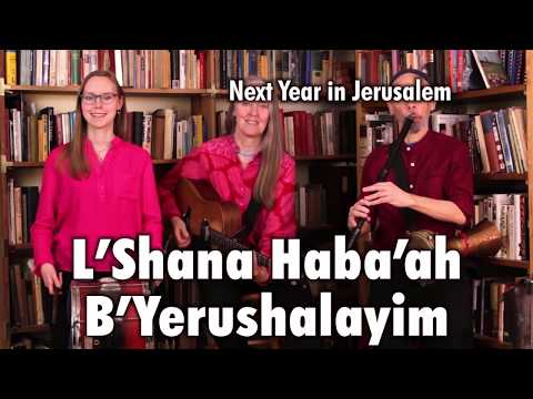 Three musicians standing in front of two bookcases, playing Bulgarian tupan, guitar, Bulgarian flute, and darabuka on “L’Shana Haba’ah B’Yerushalayim.” This is a still from a video of the Ensemble M’chaiya performing live.