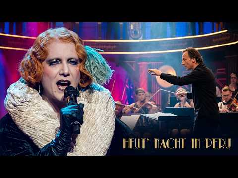 "Heut' Nacht in Peru" ["Απόψε στο Περού"], με τη Madame Le Pustra [Μαντάμ Λε Πούστρα] και τη Baltic Sea Philharmonic [Φιλαρμονική της Βαλτικής] υπό τη διεύθυνση του Kristjan Järvi [Κρίστιαν Γιάρβι], από τη συναυλία Babylon Berlin in Concert (Theater des Westens [Θέατρο της Δύσης], Βερολίνο, 2023). Η περσόνα, με πρότυπα την Anita Berber [Ανίτα Μπέρμπερ] και τη Marlene Dietrich [Μάρλενε Ντήτριχ], αναβιώνει τον ανδρόγυνο κονφερανσιέ του καμπαρέ της Βαϊμάρης. Περούκα, ψιμυθίωση, χειρονομία και φωνή συνθέτουν ένα κοινωνικό φύλο που εκτίθεται ως συνειδητή σκηνική κατασκευή.